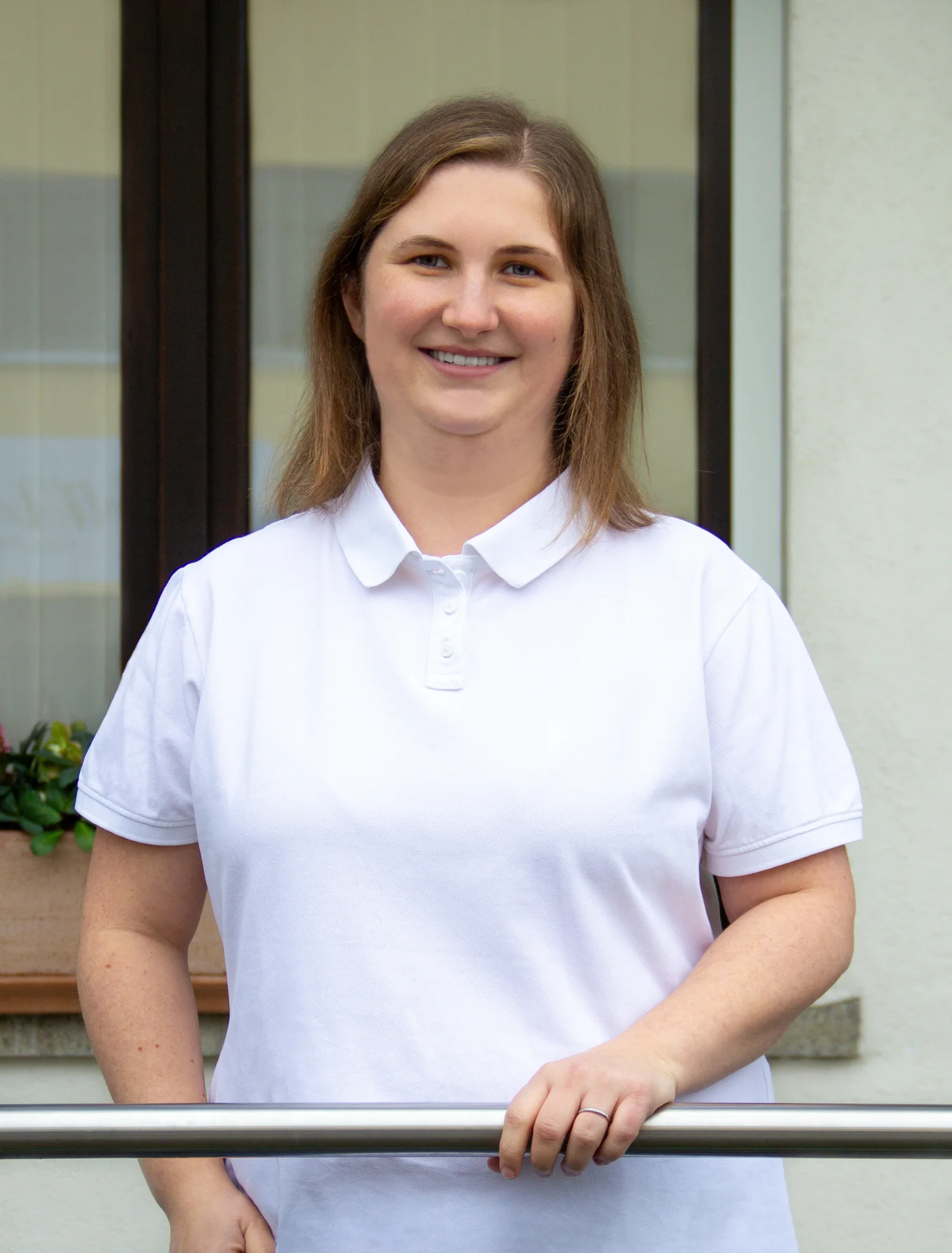 Dr. Hannah Stadler steht lächelnd am selben Geländer vor der Praxis